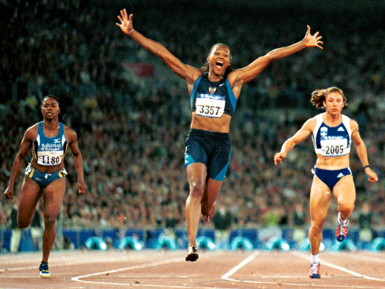 FILE - This is a Sept. 23, 2000, file photo showing Marion Jones of the United States, center, celebrating as she crosses the finish line to win the women's 100 meters at Olympic Park, during the 2000 Summer Olympics in Sydney. At left is Chandra Sturrup of the Bahamas and at right is Katerina Thanou of Greece, who won the silver. Olympic leaders reallocated two individual medals stripped from Marion Jones because of doping on Wednesday, but withheld the 100-meter gold from Greek sprinter Katerina Thanou because of her "disgraceful" behavior in evading drug tests. (AP Photo/Doug Mills, File)