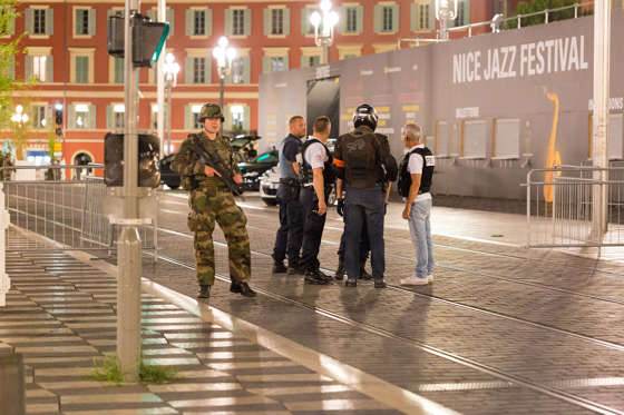 Police officers and a soldier stand by the sealed off area of an attack after a truck drove on to the sidewalk and plowed through a crowd of revelers who'd gathered to watch the fireworks in the French resort city of Nice, southern France, Friday, July 1