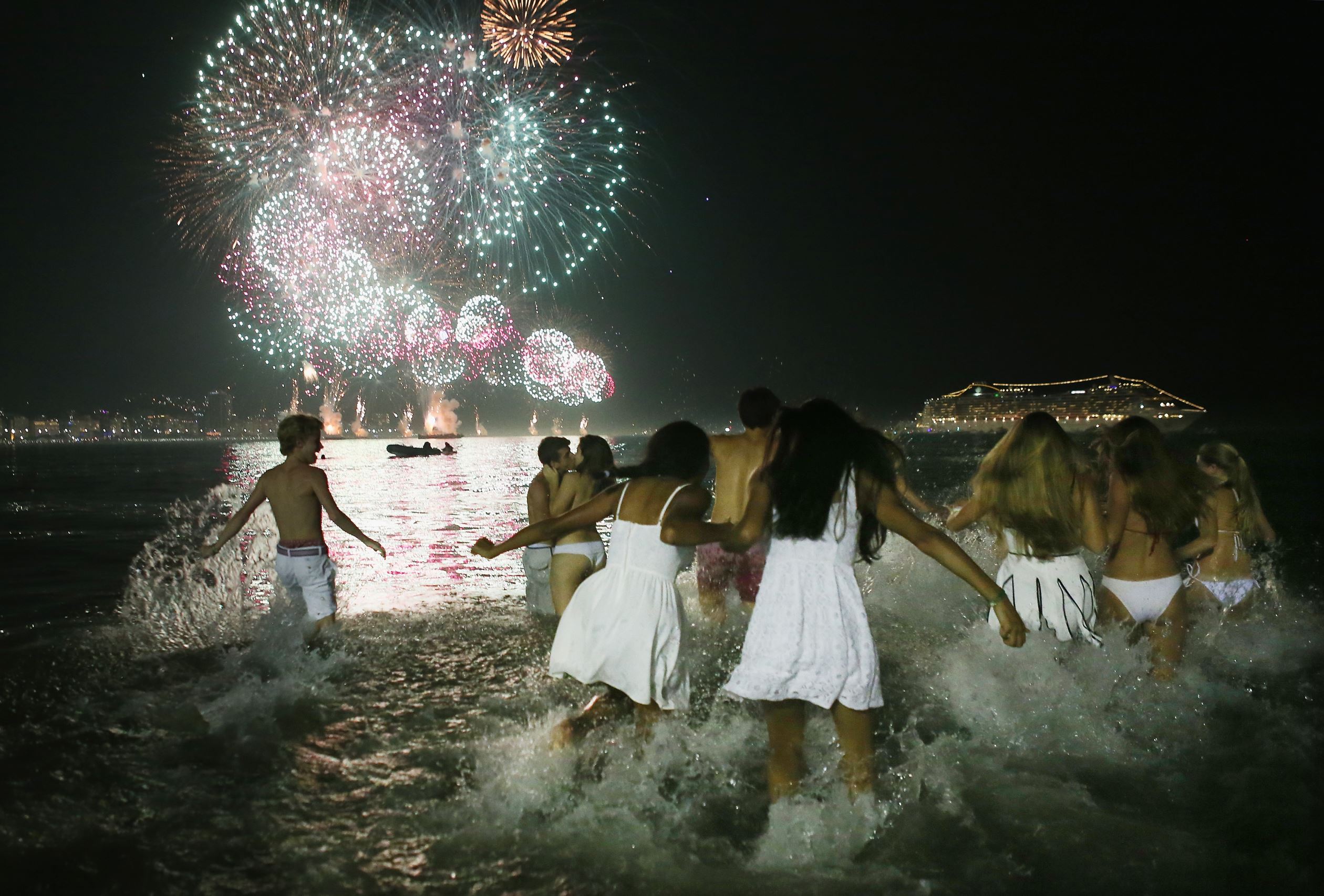 RIO DE JANEIRO, BRAZIL - JANUARY 01: Revellers dressed in white rush into the water as fireworks begin to explode to ring in the new year above Copacabana beach on January 1, 2016 in Rio de Janeiro, Brazil. More than one million people were expected to gather on Copacabana beach to watch the fireworks display ringing in the new year at midnight. The city is set to host the Rio 2016 Olympic Games in August. (Photo by Mario Tama/Getty Images)